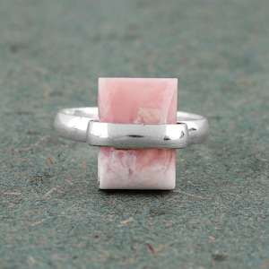 May include: A silver ring with a pink opal gemstone set in a rectangular shape.