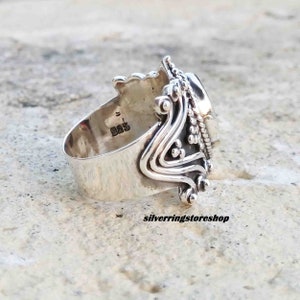 Puede incluir: Un anillo de plata con un dise&ntilde;o ornamentado y una gran piedra ovalada. El anillo est&aacute; marcado con "925" en la banda interior.