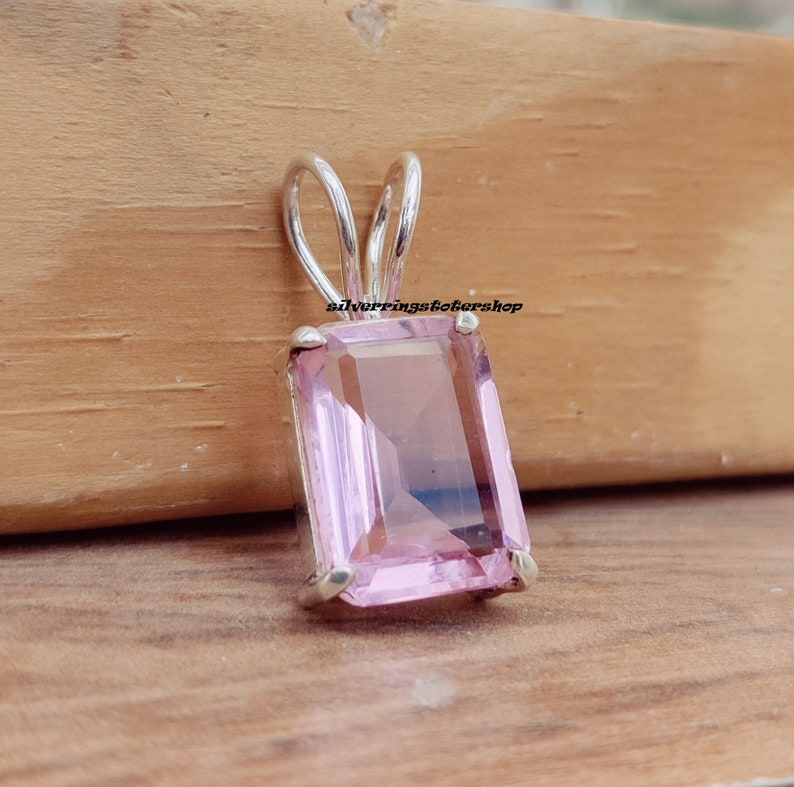 May include: A silver pendant with a light pink, rectangular gemstone. The pendant has a simple, elegant design.