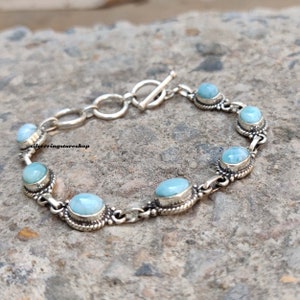 May include: A silver bracelet featuring oval and round light blue gemstones. The gemstones are set in ornate silver bezels and linked by a chain. The bracelet has a toggle clasp. The text "silverringstore shop" is visible.