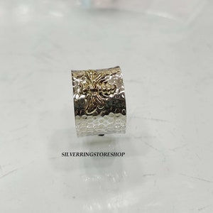 May include: A silver ring with a hammered texture and a gold bee design. The ring is wide and has a rounded shape.
