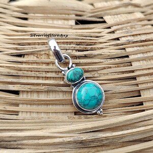 May include: Silver pendant with two turquoise stones. The larger stone is round and the smaller stone is oval. The pendant has a silver bail for attaching to a chain.