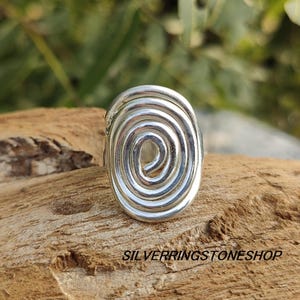 May include: A silver ring with a spiral design. The ring is oval shaped and has a smooth, polished finish.