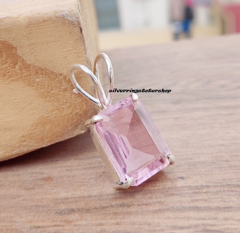 May include: A silver pendant with a light pink rectangular gemstone. The pendant has a bail for attaching to a chain.