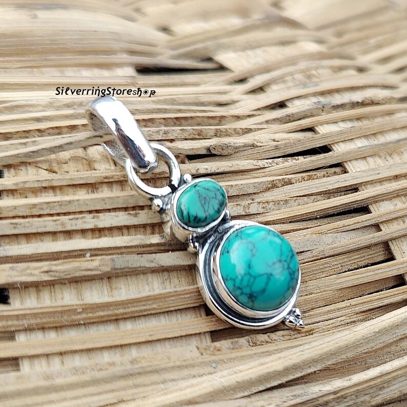 May include: Silver pendant with two turquoise stones. The larger stone is oval shaped and the smaller stone is round. The pendant has a bail for attaching to a chain.
