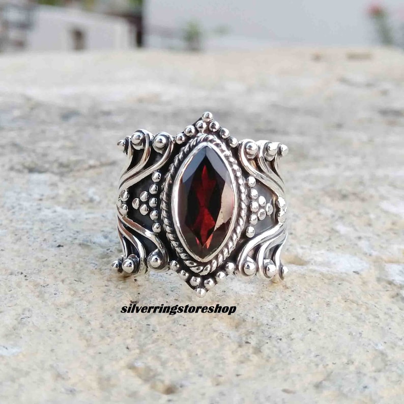 Puede incluir: Un anillo de plata con una gran piedra preciosa roja en forma de marquesa engastada en un dise&ntilde;o ornamentado y detallado. El anillo tiene una banda ancha y est&aacute; decorado con peque&ntilde;as cuentas redondas.