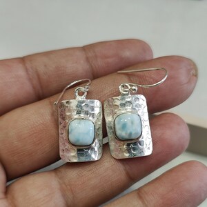 Pode incluir: Um par de brincos de prata com uma pedra preciosa azul claro de forma quadrada. Os brincos t&ecirc;m uma textura martelada.