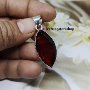 May include: A silver pendant with a large, deep red, faceted gemstone. The pendant is in the shape of a marquise.