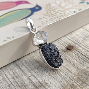 Puede incluir: Un colgante de plata con una roca volc&aacute;nica negra y dos cristales de cuarzo transparentes.