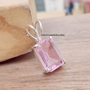 May include: A silver pendant with a light pink rectangular gemstone. The pendant has a simple bail design.