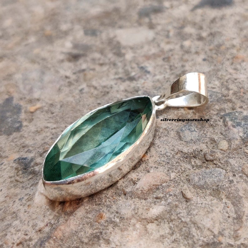 May include: A silver pendant featuring a marquise-shaped green gemstone. The pendant has a simple design and is perfect for adding a touch of elegance to any outfit.