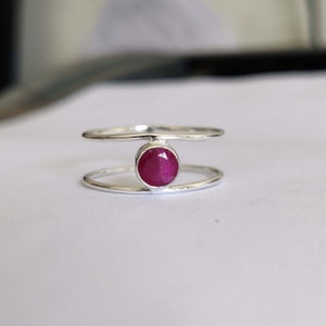 Może przedstawiać: Srebrny pierścionek z podwójnym paskiem, w którym znajduje się okrągły, czerwony kamień szlachetny.