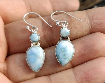 Könnte beinhalten: Ein Paar silberne Ohrhänger mit blauen und weißen, schillernden Edelsteintropfen. Die Ohrringe haben eine Tropfenform und sind mit einem kleineren runden Edelstein verziert.