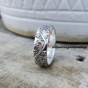 May include: A silver ring with an ornate floral design. The ring showcases a detailed pattern of flowers and vines, with a polished surface. The text "silverringstore shop" is visible on the side. This ring is a piece of jewellery.