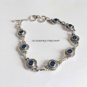 May include: A silver bracelet with a toggle clasp and blue round gemstones set in silver bezels. The bracelet has a delicate chain design.