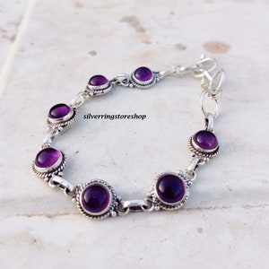 May include: A silver bracelet featuring eight round, deep purple gemstones. Each stone is set in a decorative, beaded bezel. The bracelet is connected by silver links and has a clasp closure. The text "silverringstore shop" is visible.