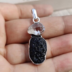 Puede incluir: Un colgante de plata con un cristal de cuarzo transparente y una roca de lava negra. El colgante est&aacute; dise&ntilde;ado en un estilo moderno y es perfecto para agregar un toque de naturaleza a cualquier atuendo.