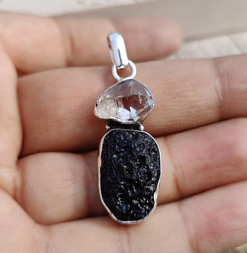 Puede incluir: Un colgante de plata con un cristal de cuarzo transparente y una roca de lava negra. El colgante est&aacute; dise&ntilde;ado en un estilo moderno y es perfecto para agregar un toque de naturaleza a cualquier atuendo.