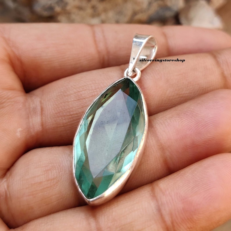 May include: A silver pendant with a large, faceted, green gemstone in a marquise shape.