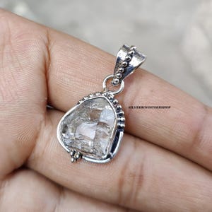 May include: A silver pendant featuring a clear quartz crystal with a faceted design. The pendant has a beaded border and a silver bail.