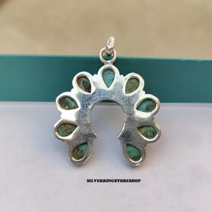 Pu&ograve; includere: Un ciondolo d'argento a forma di ferro di cavallo, ornato di pietre color turchese. Il ciondolo ha un anello nella parte superiore per una catena. Il testo "SILVERRINGSTORESHOP" &egrave; in basso.