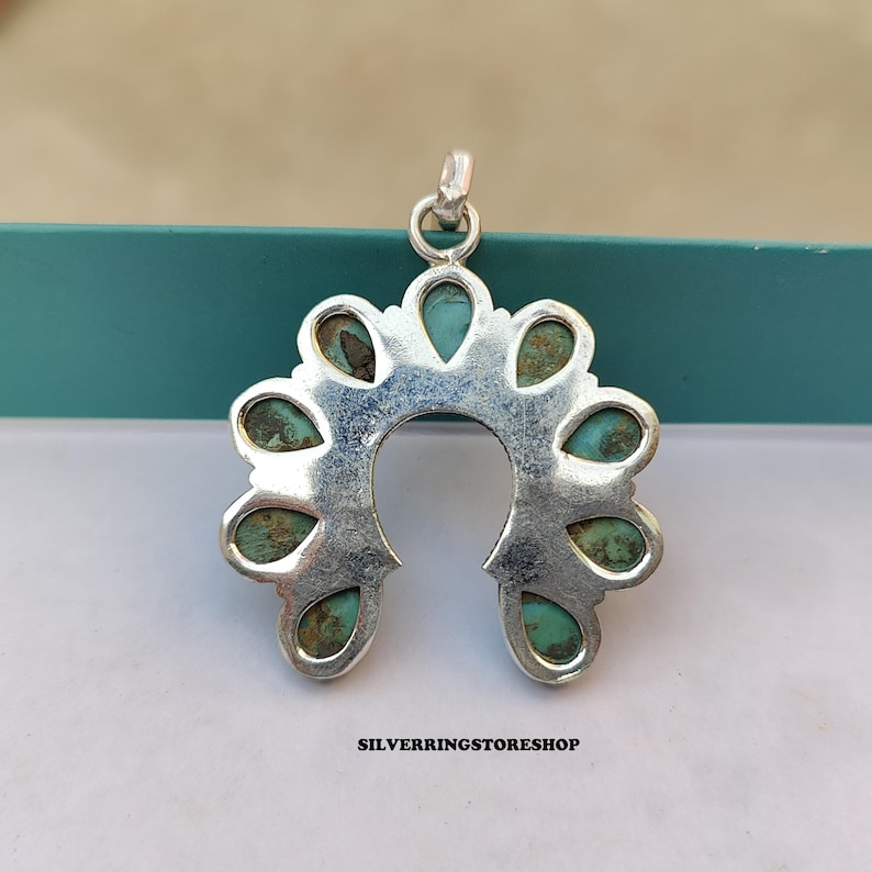 Pu&ograve; includere: Un ciondolo d'argento a forma di ferro di cavallo, ornato di pietre color turchese. Il ciondolo ha un anello nella parte superiore per una catena. Il testo "SILVERRINGSTORESHOP" &egrave; in basso.