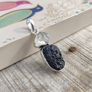 Puede incluir: Un colgante de plata con una roca volc&aacute;nica negra y dos cristales de cuarzo transparentes.