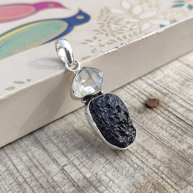 Puede incluir: Un colgante de plata con una roca volc&aacute;nica negra y dos cristales de cuarzo transparentes.