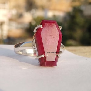 May include: A silver ring with a large, red, coffin-shaped gemstone. The text "Silverringstore shop" is visible on the ring.