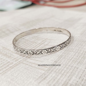 May include: A silver bangle bracelet with a floral design. The bracelet is simple and elegant, and would make a great gift for any occasion.