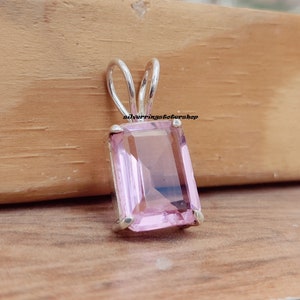 May include: A silver pendant with a light pink, rectangular gemstone. The pendant has a simple, elegant design.