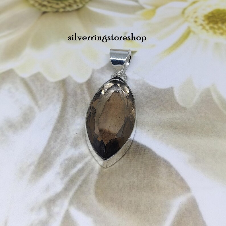 May include: A silver pendant with a marquise-shaped smoky quartz gemstone. The pendant is on a white background.