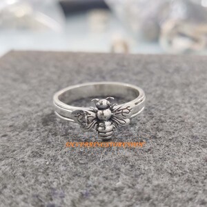 May include: A silver ring with a bee design. The bee is detailed with wings, legs, and a body.