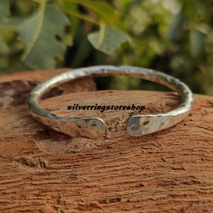 May include: A silver hammered bangle bracelet with a textured finish. The bracelet is open and has a slightly curved shape.