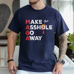 May include: A navy blue t-shirt with the text "MAKE the ASSHOLE GO AWAY" in white letters. A red tie and a red slash over the "O" in "ASSHOLE" are visible.