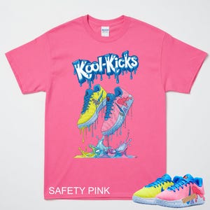 May include: A safety pink t-shirt featuring a graphic of two trainers with the text "Kool-Kicks". The trainers are yellow and pink with blue details, and the text "SAFETY PINK" is printed at the bottom.