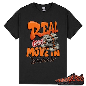 May include: A black short-sleeve t-shirt featuring a graphic print with the orange text "REAL", "ONES" in red, and "MOVE IN SILENCE" in orange. A stack of US dollar bills is illustrated above the text. A black and orange tiger-striped sneaker is shown.