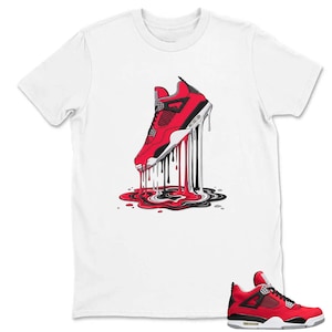 May include: White t-shirt featuring a graphic of a red and black sneaker with dripping paint. The sneaker design includes black laces, a white sole, and a red upper. The dripping paint effect includes red, black, and white colors.