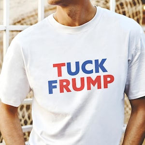 May include: White t-shirt with the text "TUCK FRUMP" printed in blue and red letters.