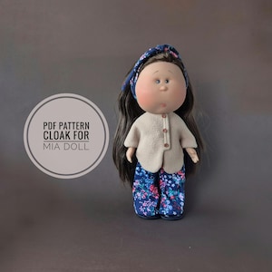 May include: A handmade doll wearing a blue floral headband, a beige button-up jacket, and blue floral trousers. The doll has long dark hair and a round face. Text on the left side reads "PDF PATTERN CLOAK FOR MIA DOLL."