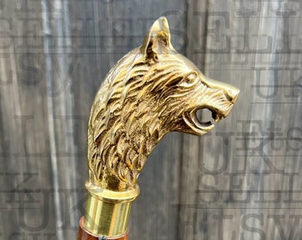 May include: A wooden walking stick with a brass wolf head handle. The stick has a brown wooden shaft and a brass ferrule. A black tag is attached to the stick with the text "UK Etsy Seller Delivery With In 3 Days" and the website address "www.ministryofantiques.etsy.com".