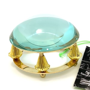 Może przedstawiać: Antyczne szkło powiększające z okrągłą, jasnoniebieską soczewką i złotą metalową podstawą z czterema ozdobnymi nóżkami. Podstawa ma kształt pierścienia. Szkło powiększające znajduje się na białym tle. Obraz zawiera również czarno-białą etykietę z tekstem "Ministry of Antiques UK Seller Same Day Dispatch".