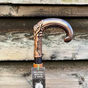 May include: A copper-colored walking stick with a detailed tree design on the handle. The stick has a wooden shaft and a tag that says "Delivery with in 3 days" and "Ministry of Antiques UK Seller Same Day Dispatch".