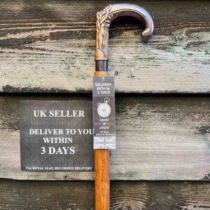 May include: A wooden walking stick with a copper-colored handle featuring a tree design. The handle is curved and has a black metal band. The stick is labeled "UK Seller" and "Delivery within 3 days".