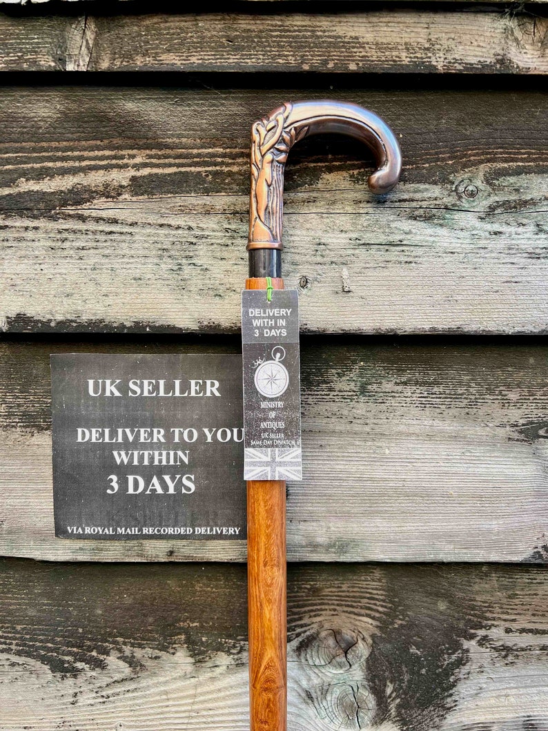 May include: A wooden walking stick with a copper-colored handle featuring a tree design. The handle is curved and has a black metal band. The stick is labeled "UK Seller" and "Delivery within 3 days".