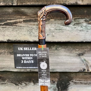 May include: A wooden walking stick with a copper-colored handle featuring a tree design. The handle has a curved top and a black metal band. A tag attached to the stick reads "Delivery with in 3 days" and "Ministry of Antiques UK Seller Same Day Dispatch".