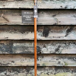 May include: A wooden walking stick with a silver handle featuring a floral design. The stick has a brown finish and a black rubber tip. The stick is leaning against a wooden wall.
