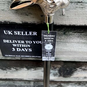 May include: A silver walking stick with a rabbit head handle. The stick is black and has a silver band around the handle. The stick is displayed against a wooden background. The text on the tag reads "UK Seller, Deliver to you within 3 days, Via Royal Mail Recorded Delivery, Delivery within 3 days, Ministry of Antiques, UK Seller, Same Day Dispatch".