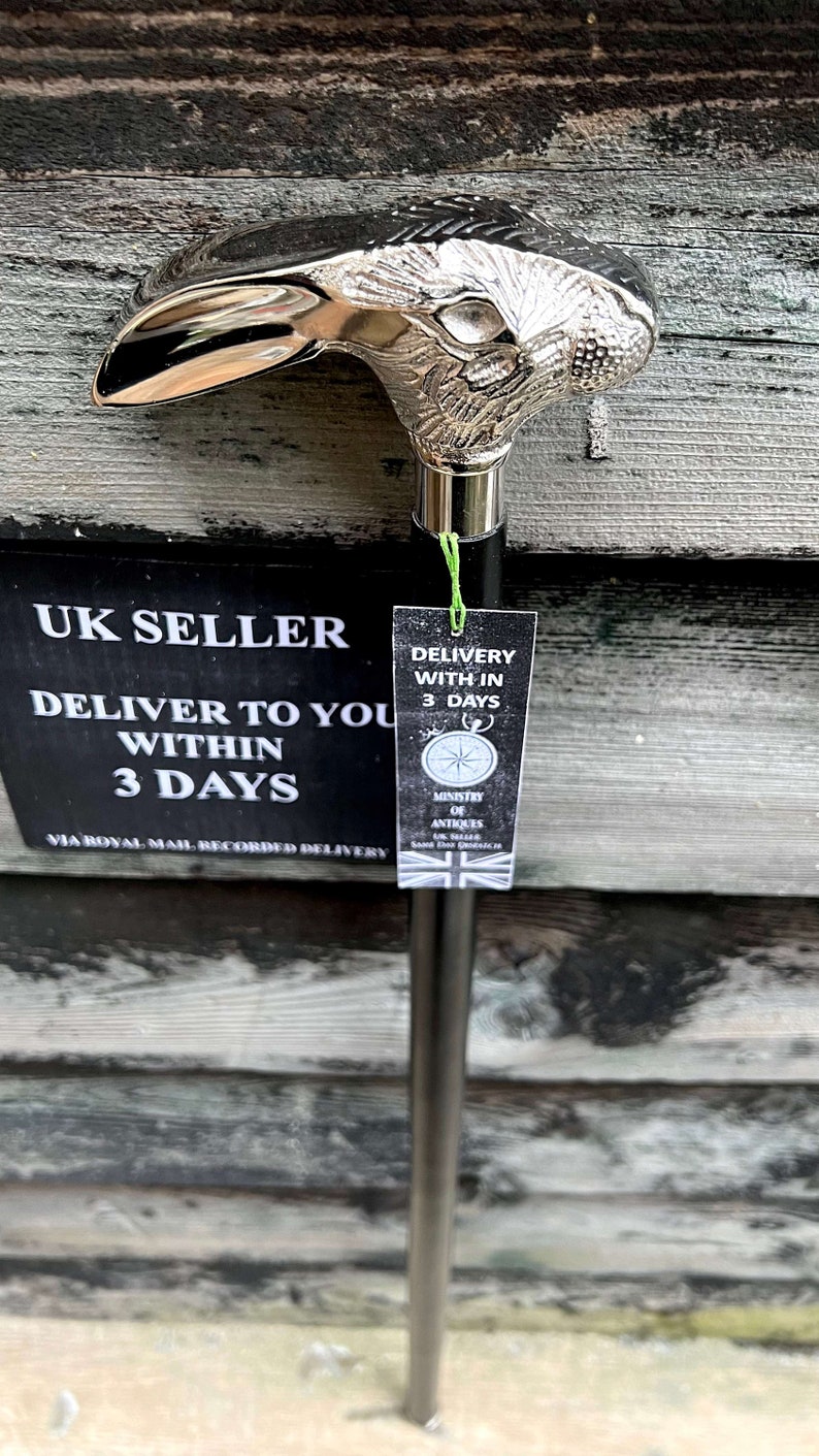 May include: A silver walking stick with a rabbit head handle. The stick is black and has a silver band around the handle. The stick is displayed against a wooden background. The text on the tag reads "UK Seller, Deliver to you within 3 days, Via Royal Mail Recorded Delivery, Delivery within 3 days, Ministry of Antiques, UK Seller, Same Day Dispatch".