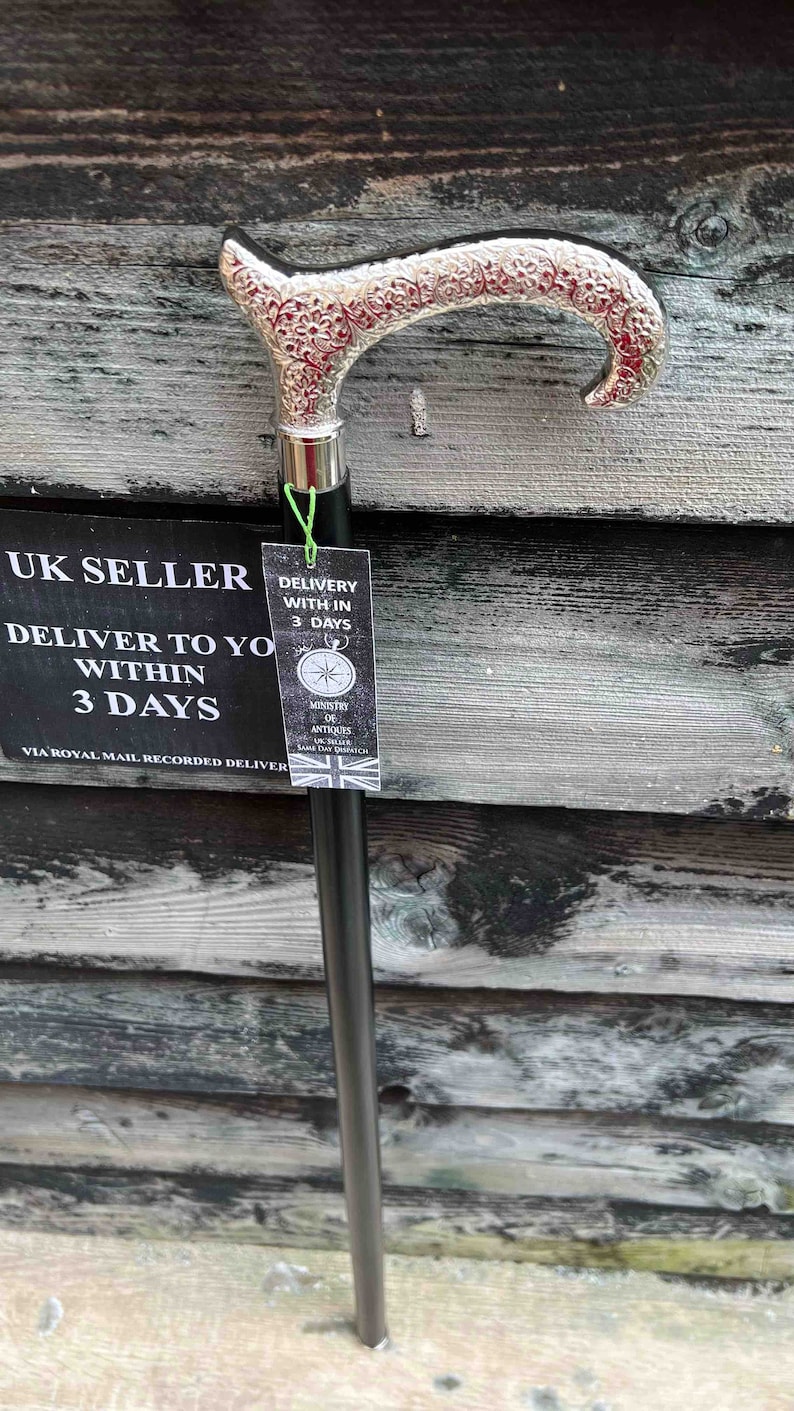 K&ouml;nnte beinhalten: Ein Gehstock aus schwarzem Holz mit einer silberbeschichteten Grifffl&auml;che. Der Griff ist mit einem komplizierten Blumenmuster verziert. Der Stock lehnt an einer Holzwand mit einem Schild, auf dem steht "UK SELLER DELIVER TO YOU WITHIN 3 DAYS VIA ROYAL MAIL RECORDED DELIVERY".